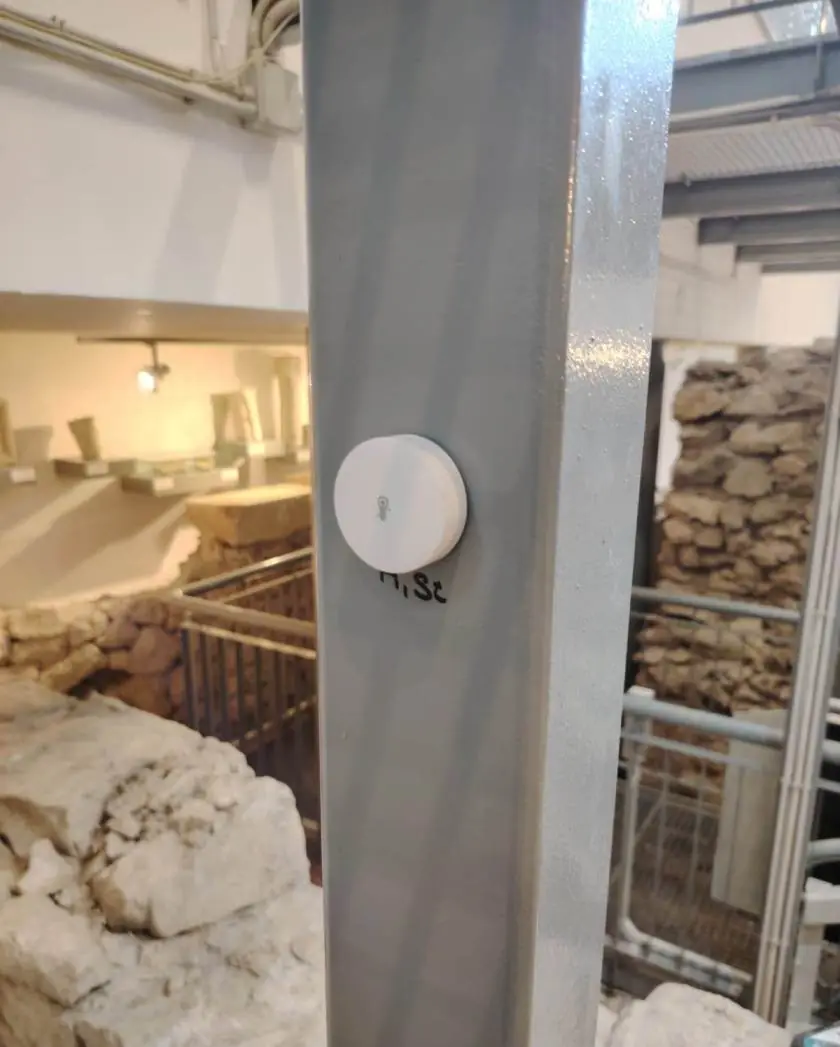 Bijeli okrugli senzor na čeličnom stupu, a iza njega kameni zid u Arheološkom muzeju Narona